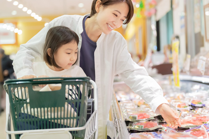 スーパーで刺身のパックを手に取る大人と子ども